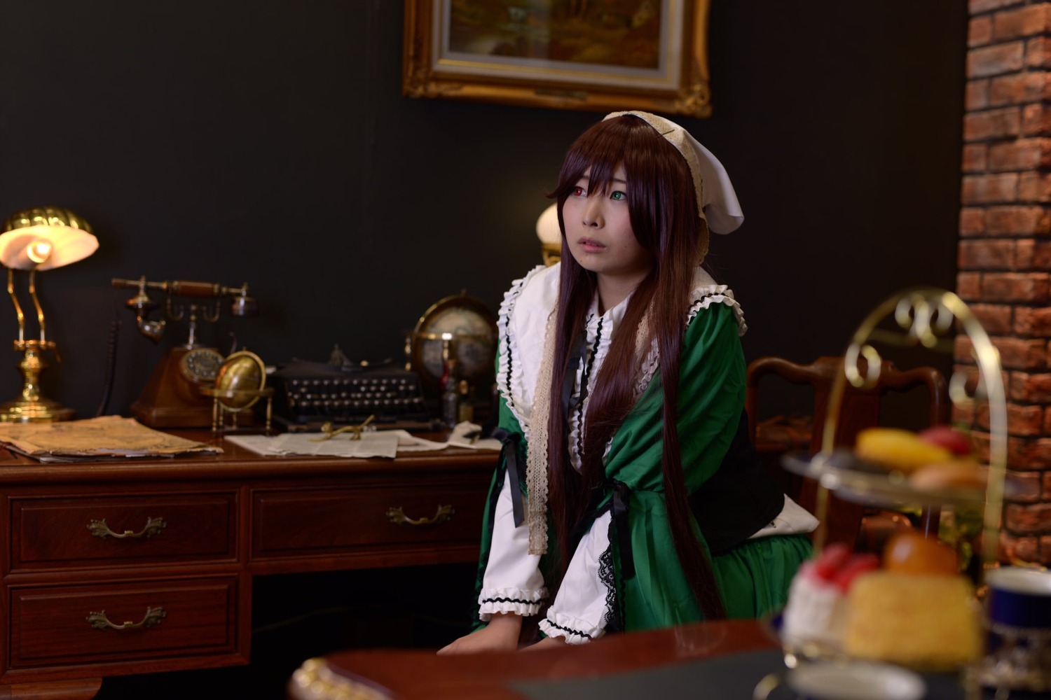 1girl blurry blurry_foreground brown_hair depth_of_field dress frills green_dress green_eyes indoors lips long_hair sitting solo suiseiseki