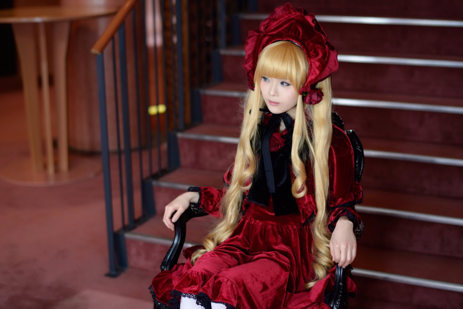 1girl bangs blonde_hair blue_eyes blurry bonnet depth_of_field dress flower long_hair looking_at_viewer red_dress shinku sitting solo twintails