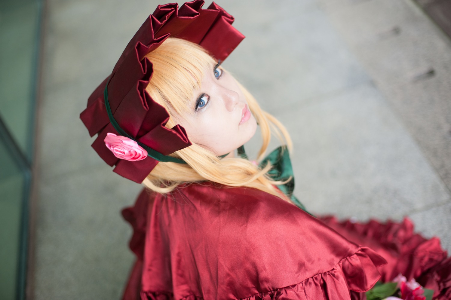 1girl bangs blonde_hair blue_eyes blurry blurry_background bonnet bow capelet depth_of_field dress flower lips long_hair looking_at_viewer photo red_capelet red_dress rose shinku solo upper_body