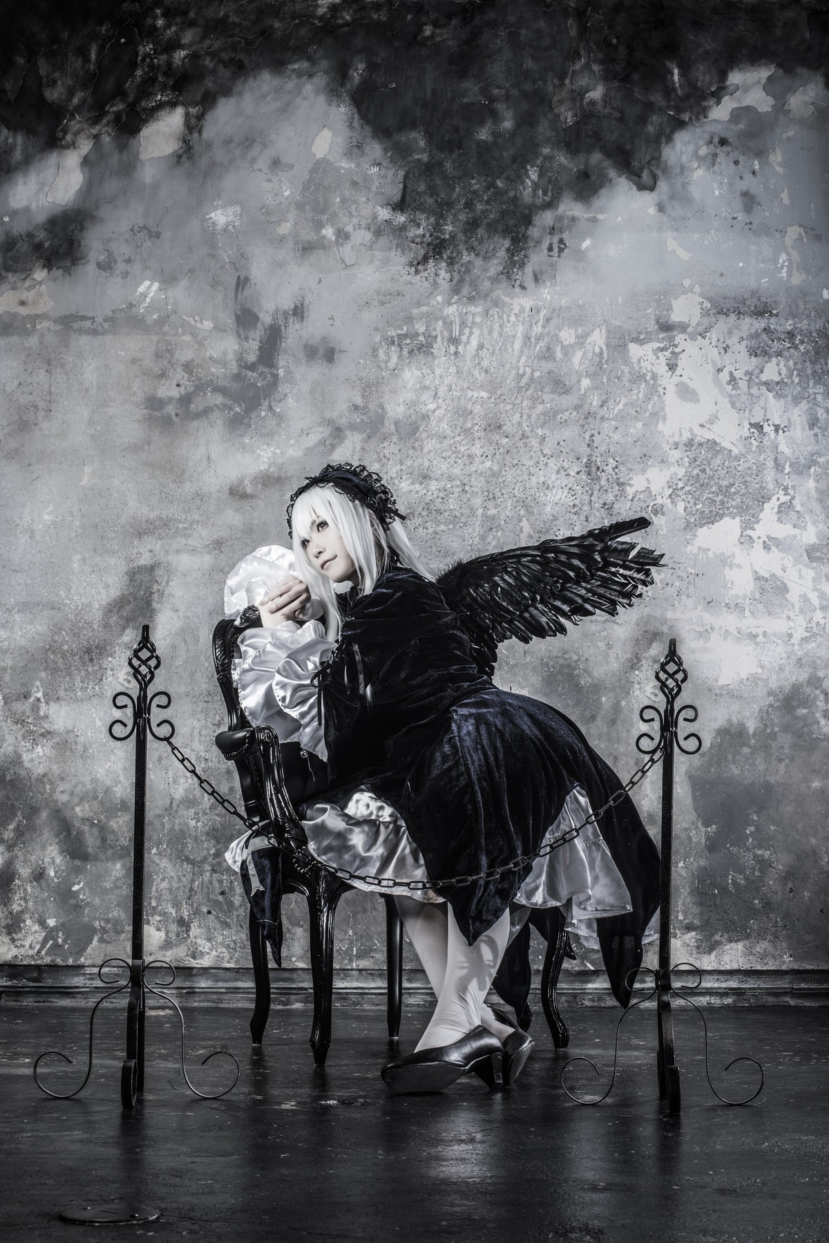 1girl black_wings boots dress feathered_wings greyscale hairband long_hair long_sleeves looking_at_viewer monochrome sitting solo standing suigintou wings