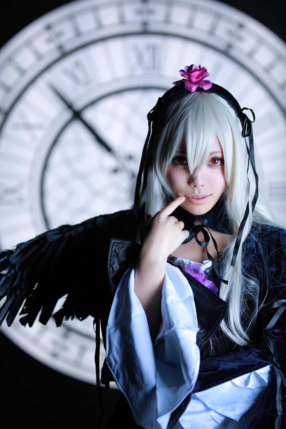 1girl blurry blurry_background blurry_foreground closed_mouth depth_of_field dress finger_to_mouth flower gothic_lolita hairband index_finger_raised long_hair long_sleeves looking_at_viewer red_eyes silver_hair solo suigintou upper_body wide_sleeves wings