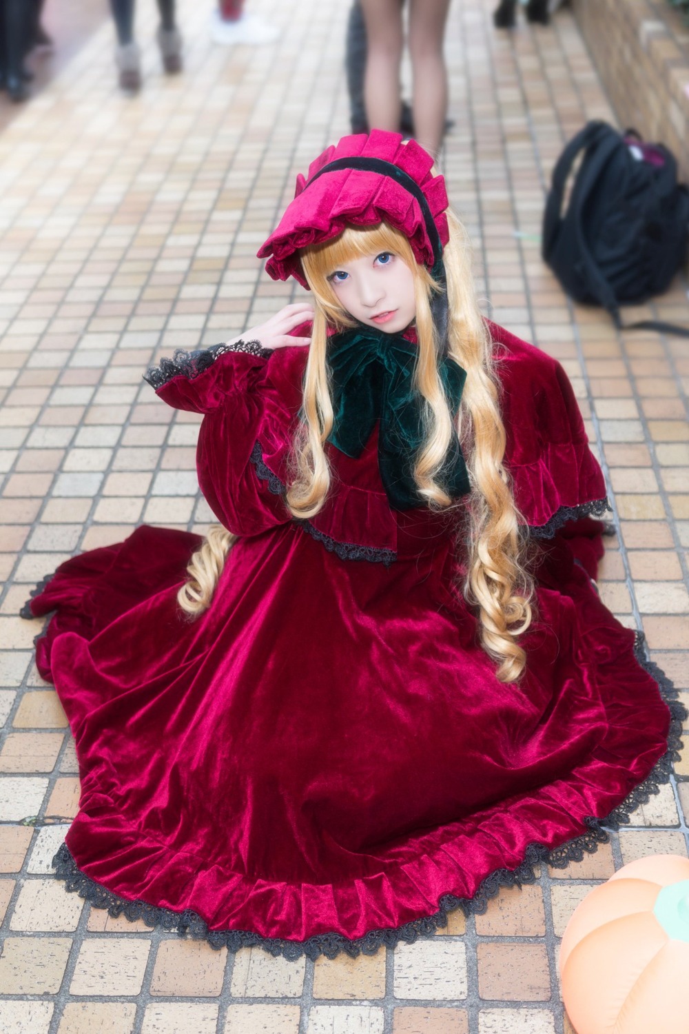 1girl blonde_hair blue_eyes blurry blurry_background blurry_foreground chain-link_fence depth_of_field dress drill_hair fence floor hat long_hair long_sleeves looking_at_viewer photo red_dress shinku sitting solo tile_floor tiles