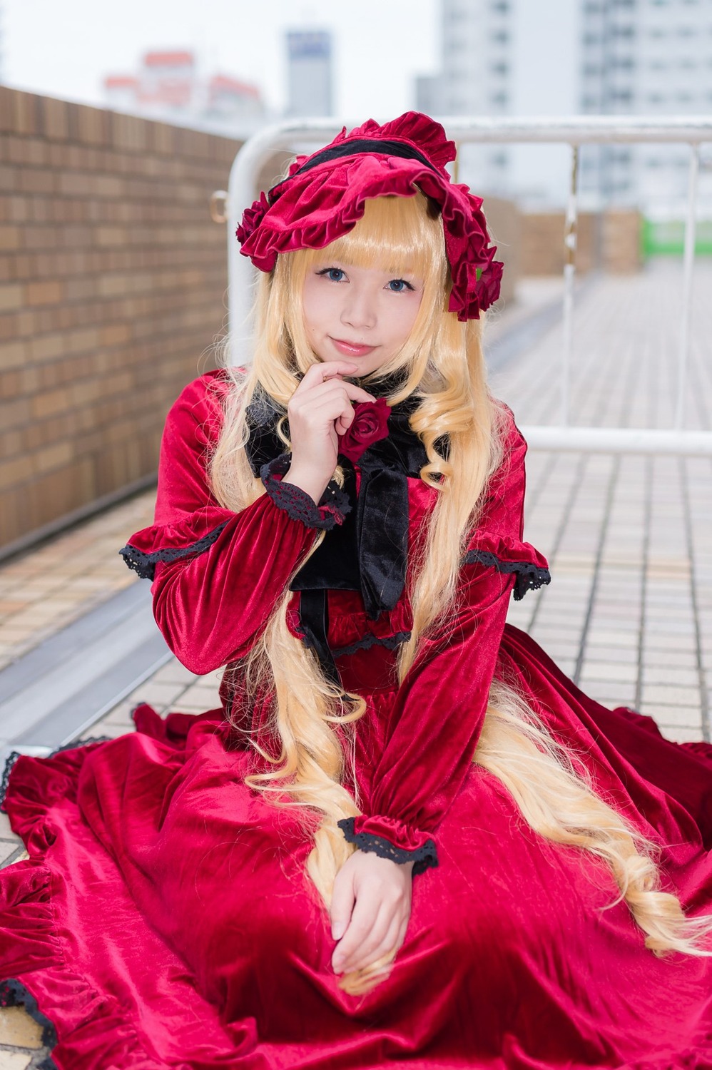 1girl blonde_hair blue_eyes blurry blurry_background building depth_of_field dress flower frills long_hair long_sleeves looking_at_viewer photo red_dress rose shinku sitting solo