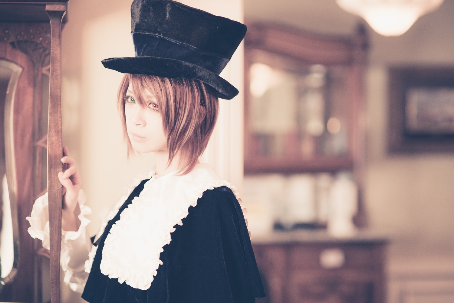 1girl blue_headwear blurry blurry_background blurry_foreground brown_hair capelet depth_of_field green_eyes hat indoors long_sleeves looking_at_viewer short_hair solo souseiseki top_hat