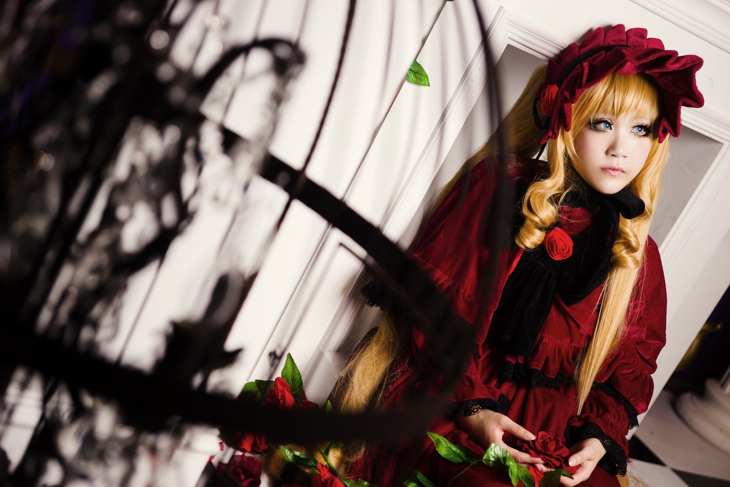 1girl bangs blonde_hair blue_eyes blurry blurry_foreground bonnet depth_of_field dress flower long_hair long_sleeves looking_at_viewer red_dress rose shinku sitting solo