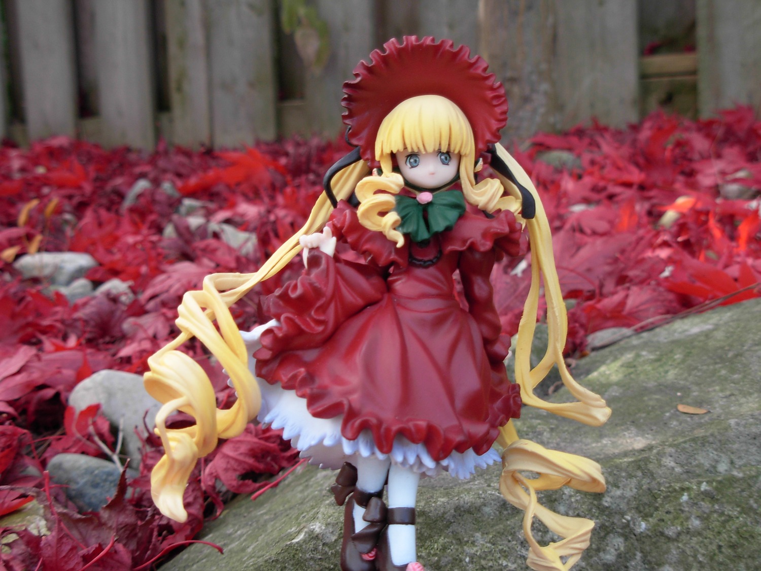 1girl auto_tagged blonde_hair blue_eyes blurry bow bowtie capelet depth_of_field doll dress drill_hair frills long_hair long_sleeves looking_at_viewer outdoors pantyhose shinku shoes sitting solo standing twintails very_long_hair white_legwear