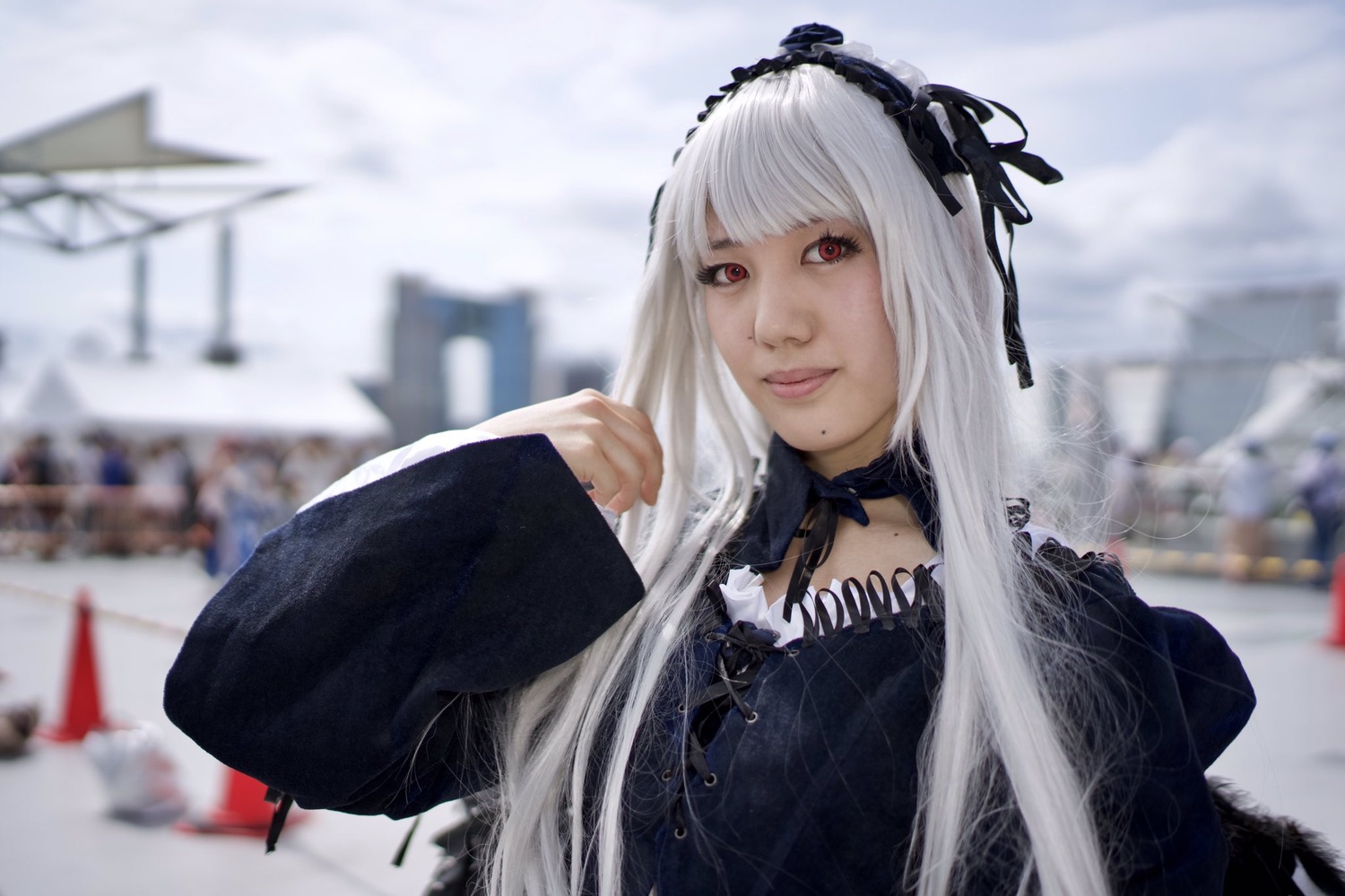1girl 3d bangs black_ribbon blurry blurry_background blurry_foreground building city closed_mouth day depth_of_field dress gothic_lolita hairband lace lips lolita_fashion long_hair long_sleeves looking_at_viewer photo red_eyes ribbon solo suigintou