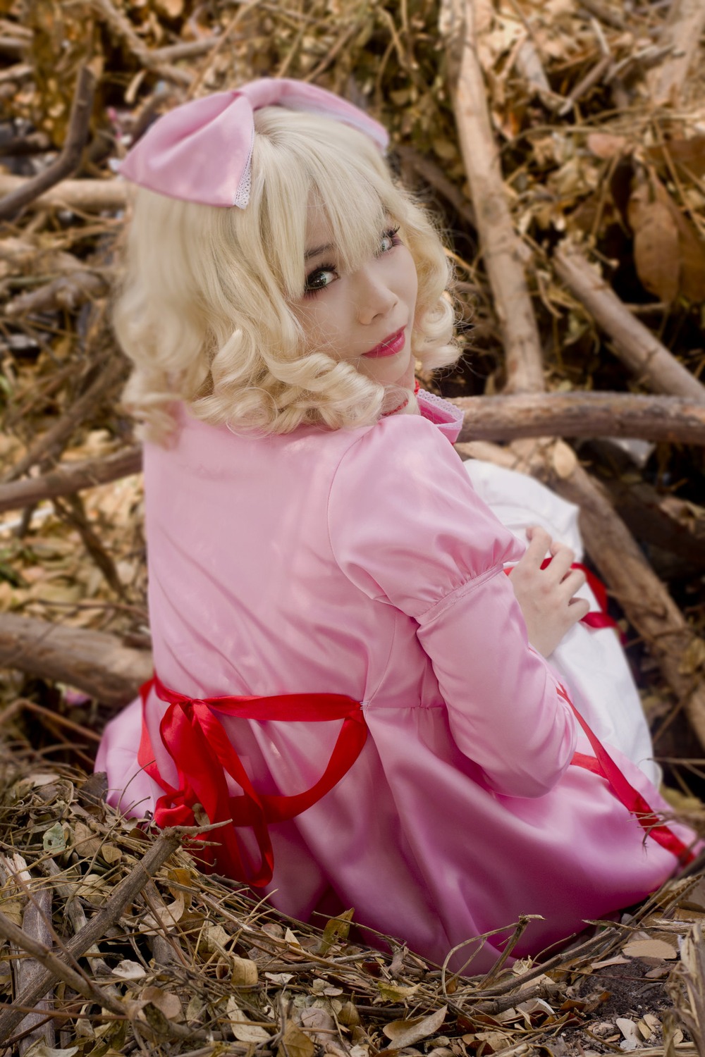 1girl blonde_hair blue_eyes blurry bow depth_of_field dress hair_bow hinaichigo lips looking_at_viewer looking_back outdoors pink_dress realistic sitting solo