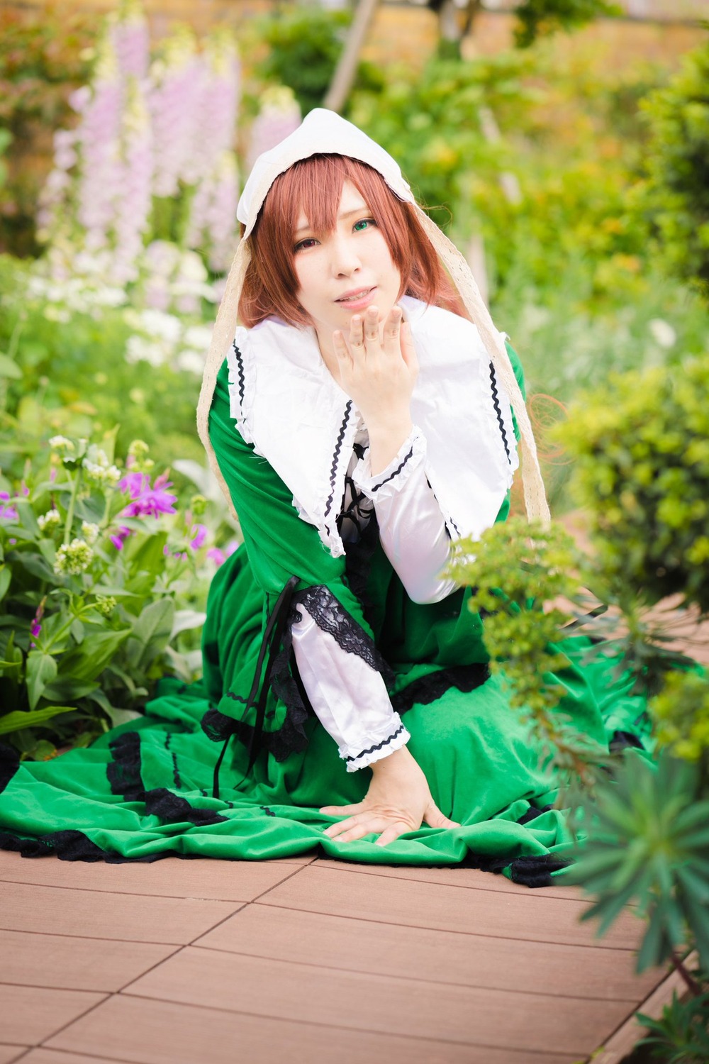 1girl blurry blurry_background blurry_foreground brown_hair depth_of_field dress flower green_dress green_eyes head_scarf lips long_sleeves one_eye_closed outdoors photo smile solo suiseiseki