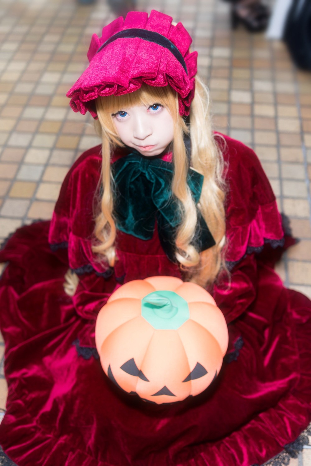 1girl blonde_hair blue_eyes blurry blurry_background blurry_foreground bonnet depth_of_field dress hat jack-o'-lantern long_hair long_sleeves looking_at_viewer photo red_dress shinku sitting solo