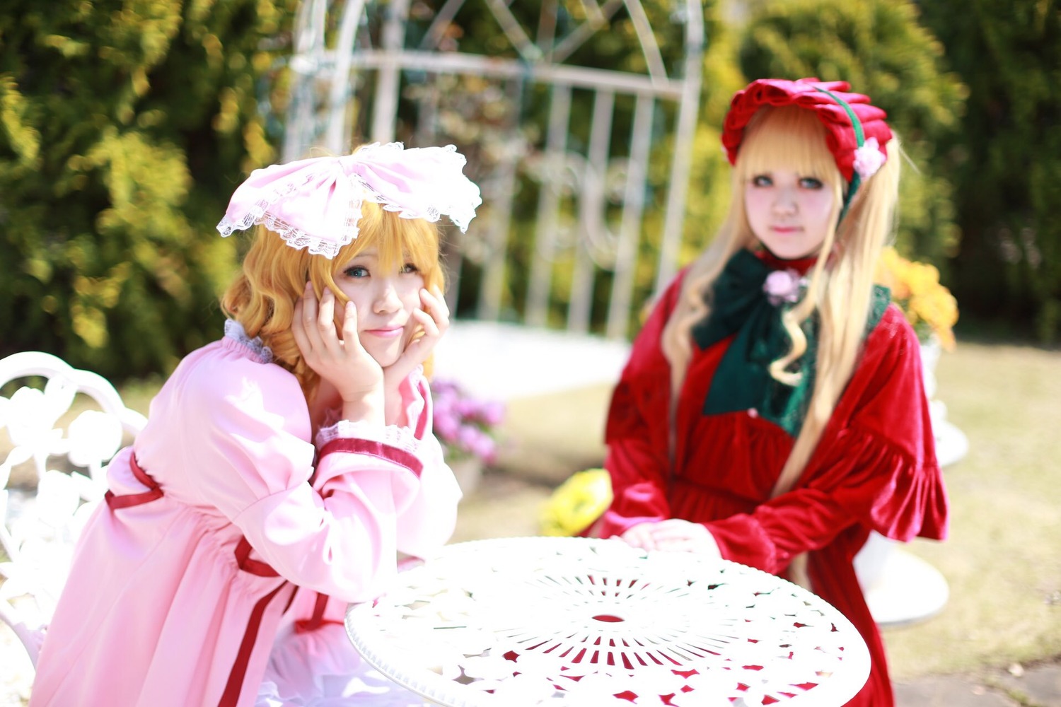 2girls blonde_hair blue_eyes blurry blurry_background bow depth_of_field dress hat long_sleeves multiple_cosplay multiple_girls photo short_hair sitting table tagme