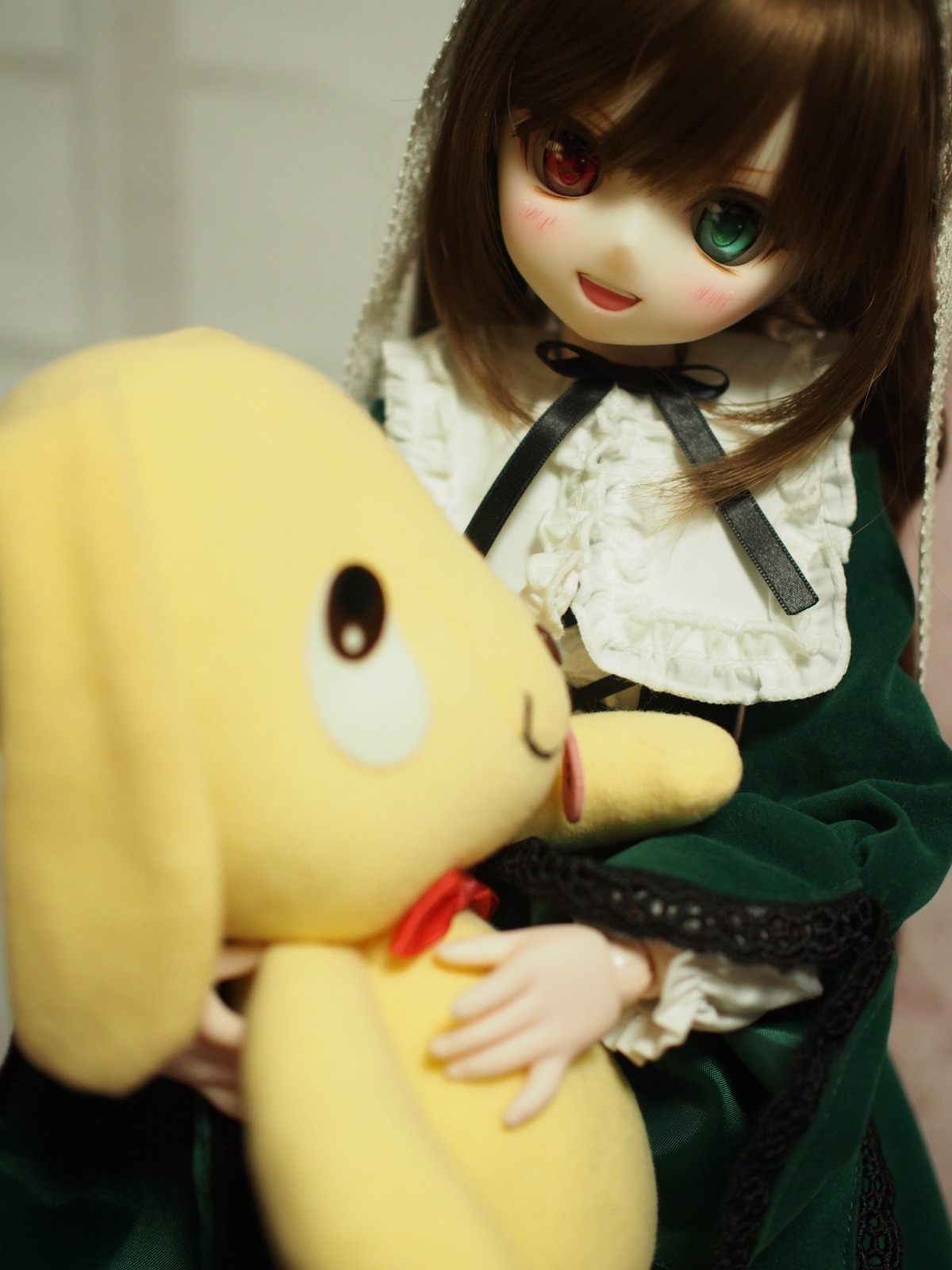 1girl :d bangs blurry blurry_foreground brown_hair depth_of_field doll dress heterochromia holding long_hair long_sleeves looking_at_viewer open_mouth red_eyes smile solo stuffed_animal suiseiseki