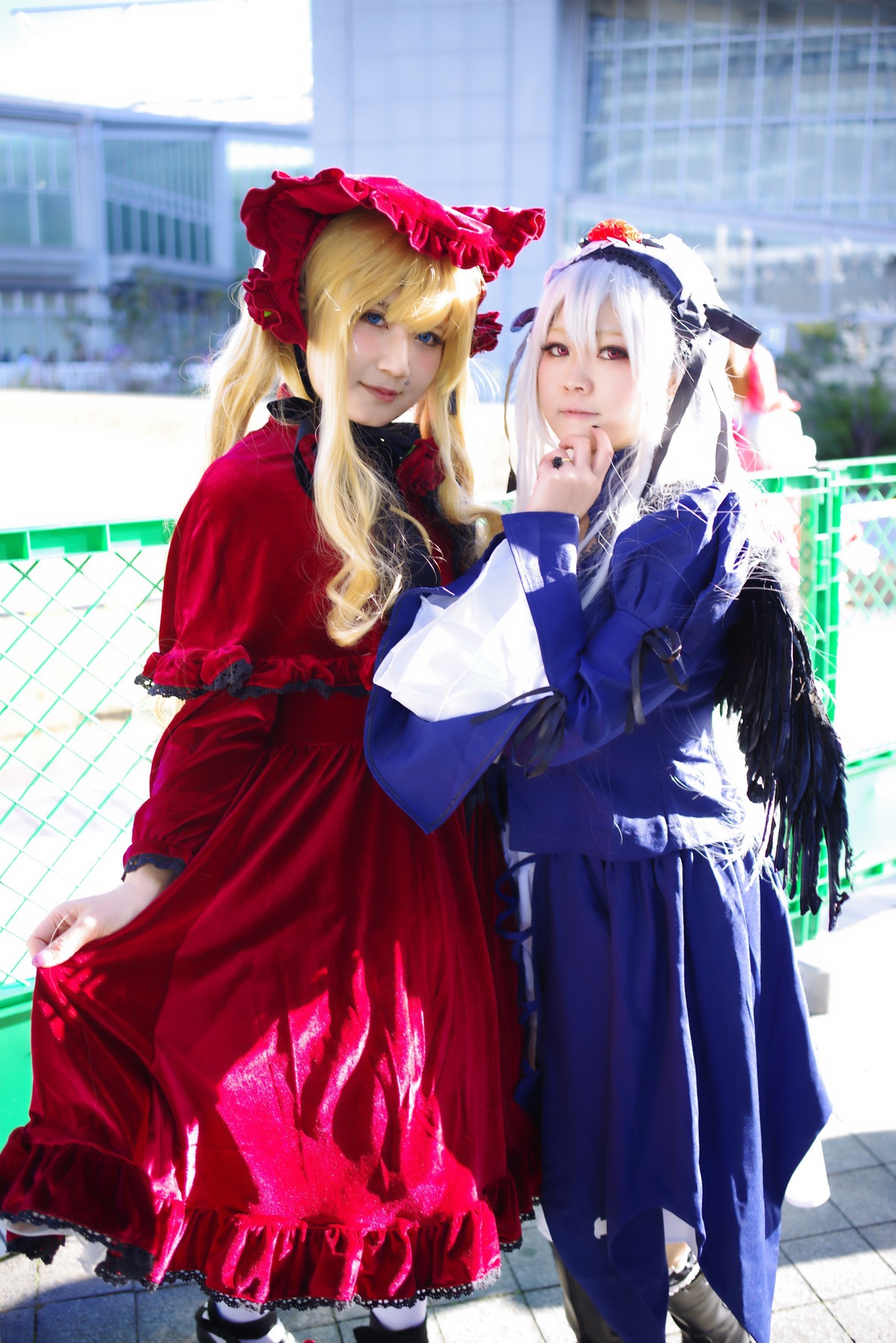 2girls blonde_hair blue_eyes blurry blurry_background bonnet building depth_of_field dress feathers fence flower frills long_hair long_sleeves looking_at_another multiple_cosplay multiple_girls red_dress rose shinku stained_glass suigintou tagme tile_floor tiles window