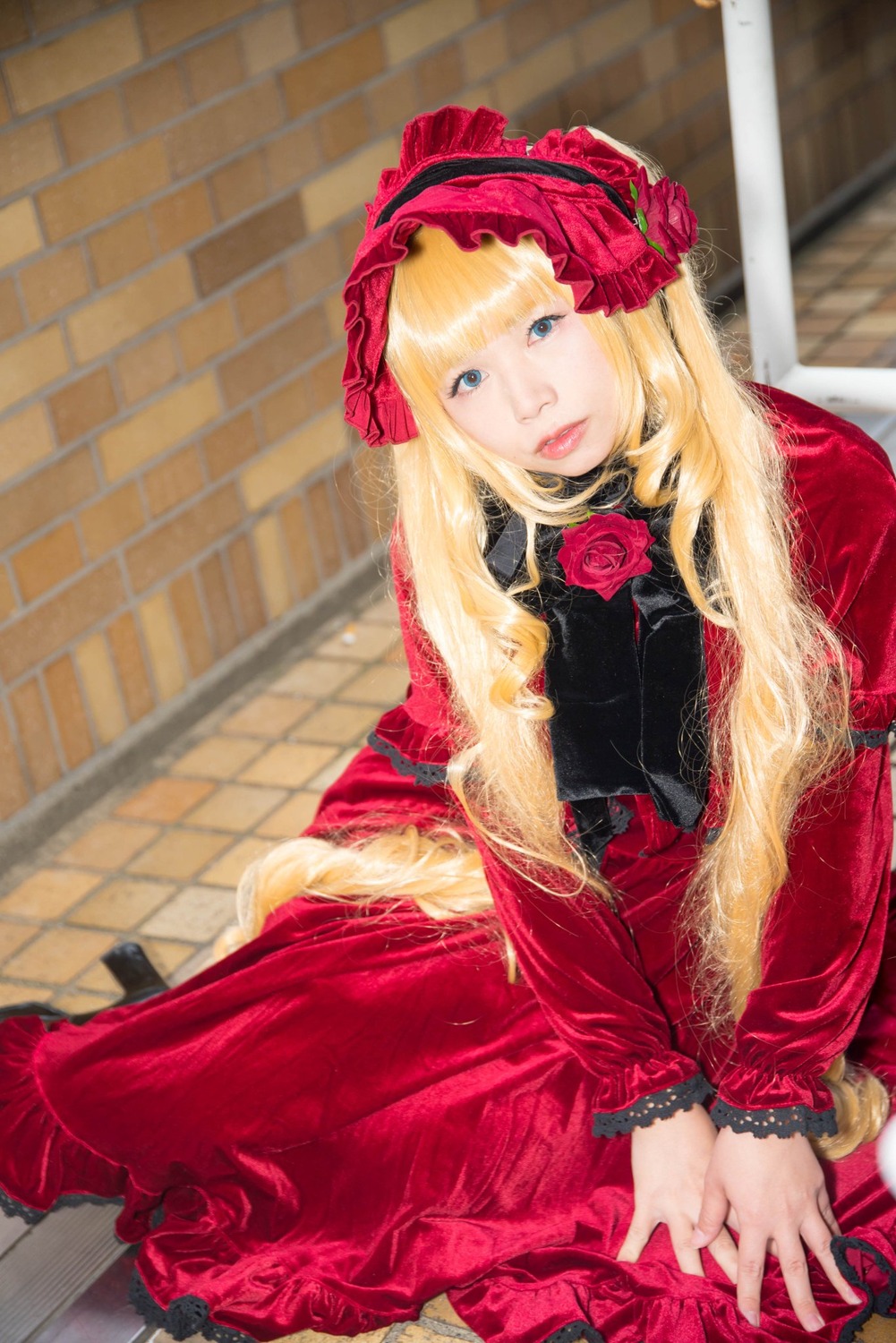 1girl blonde_hair blue_eyes brick_wall dress flower frills lips lolita_fashion long_hair long_sleeves looking_at_viewer pink_flower pink_rose red_capelet red_dress red_flower red_rose rose shinku sitting solo tiles