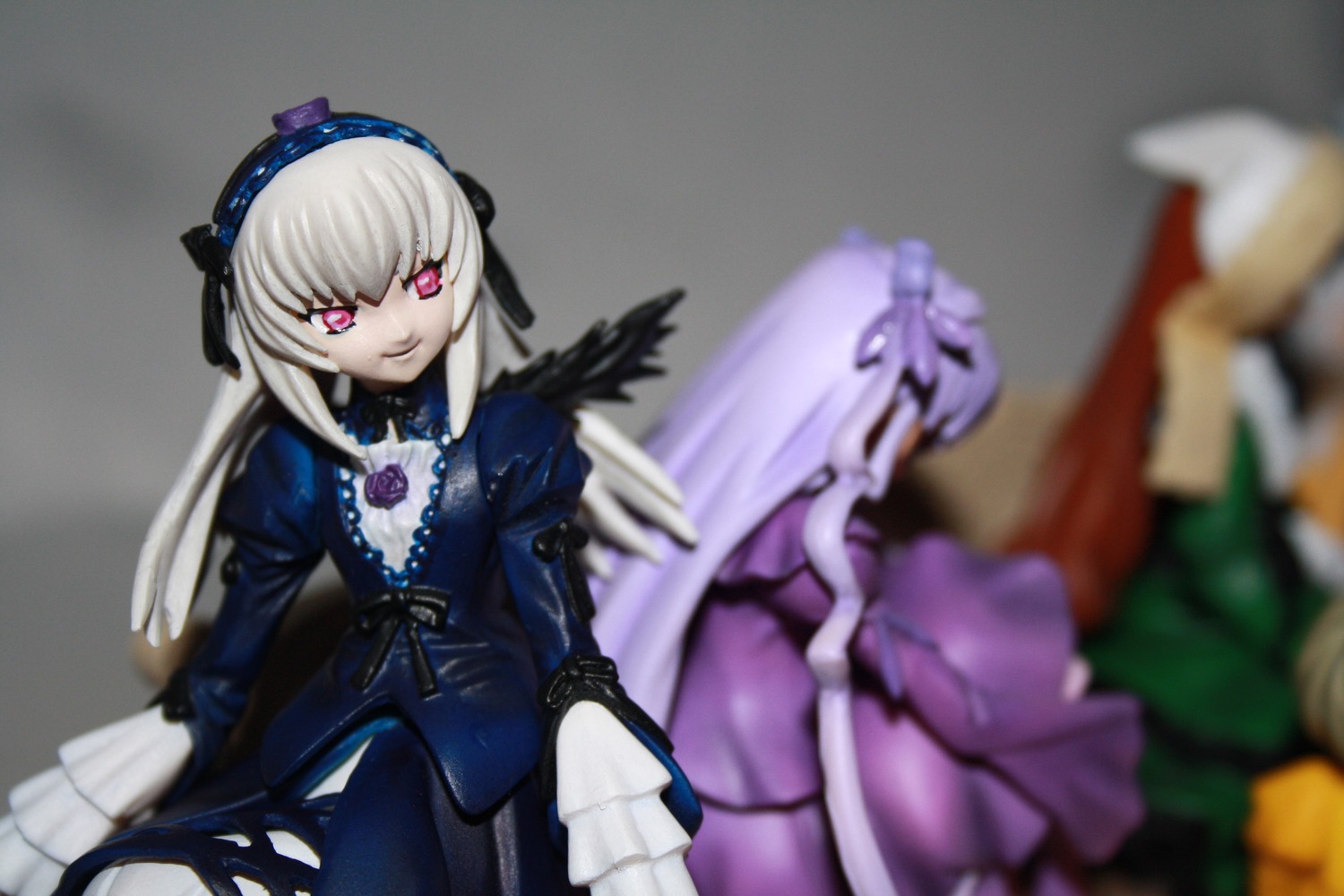 2girls 3d black_wings blurry blurry_background blurry_foreground depth_of_field doll dress figure frills hairband lolita_hairband long_hair long_sleeves looking_at_viewer motion_blur multiple_dolls multiple_girls photo silver_hair suigintou tagme wings