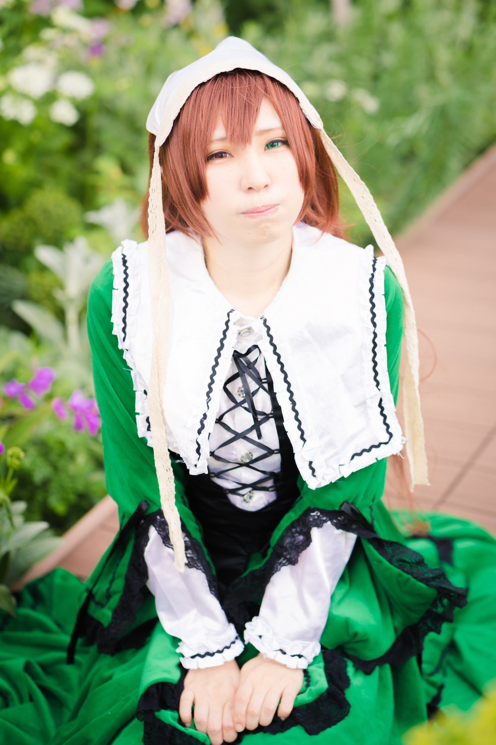 1girl bangs blurry blurry_background blurry_foreground brown_hair depth_of_field dress flower green_dress green_eyes head_scarf lips long_sleeves looking_at_viewer outdoors photo solo suiseiseki