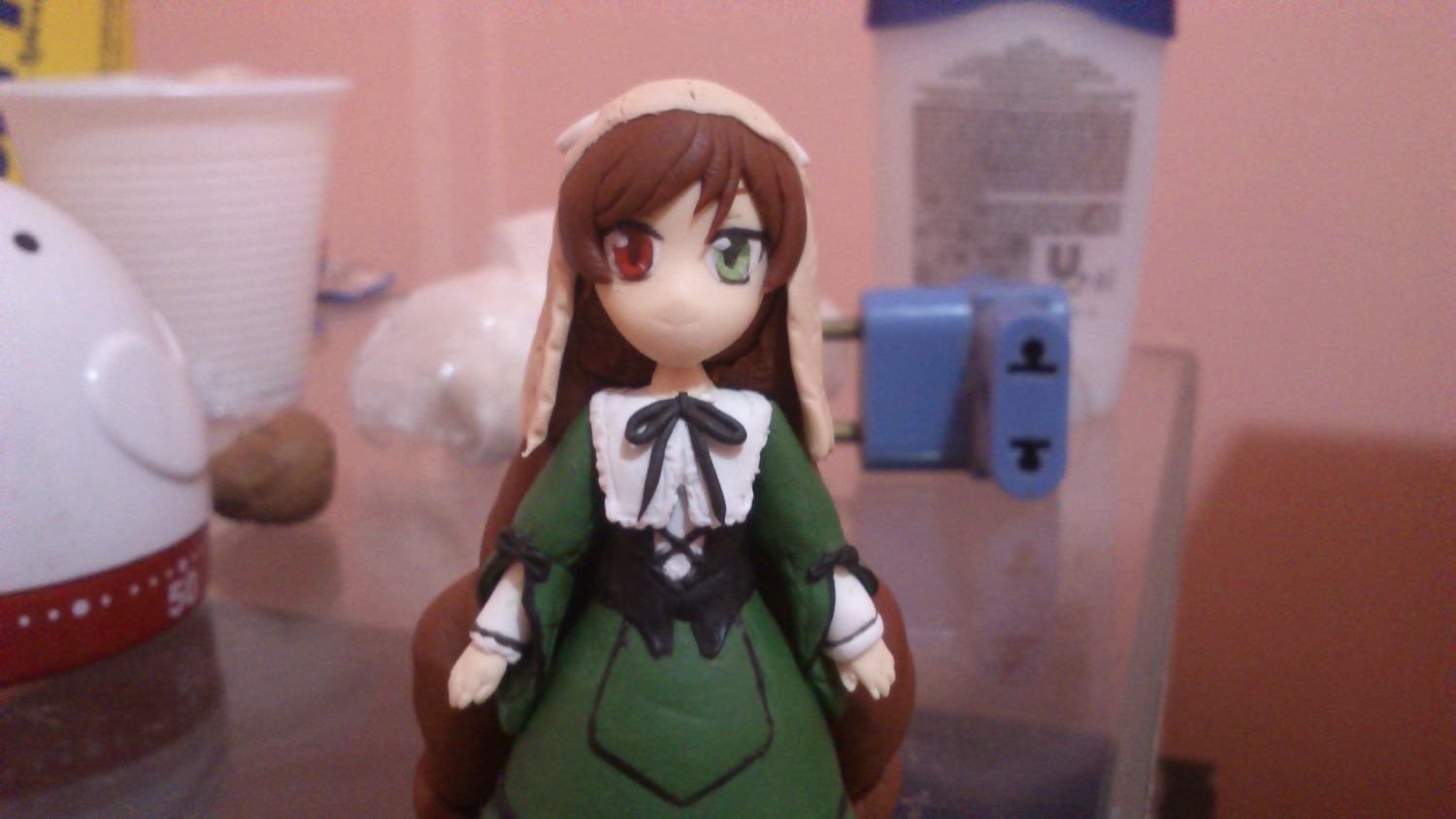 1girl blurry blurry_background blurry_foreground brown_hair depth_of_field doll dress frills green_dress green_eyes heterochromia long_hair long_sleeves looking_at_viewer red_eyes solo standing suiseiseki very_long_hair watering_can