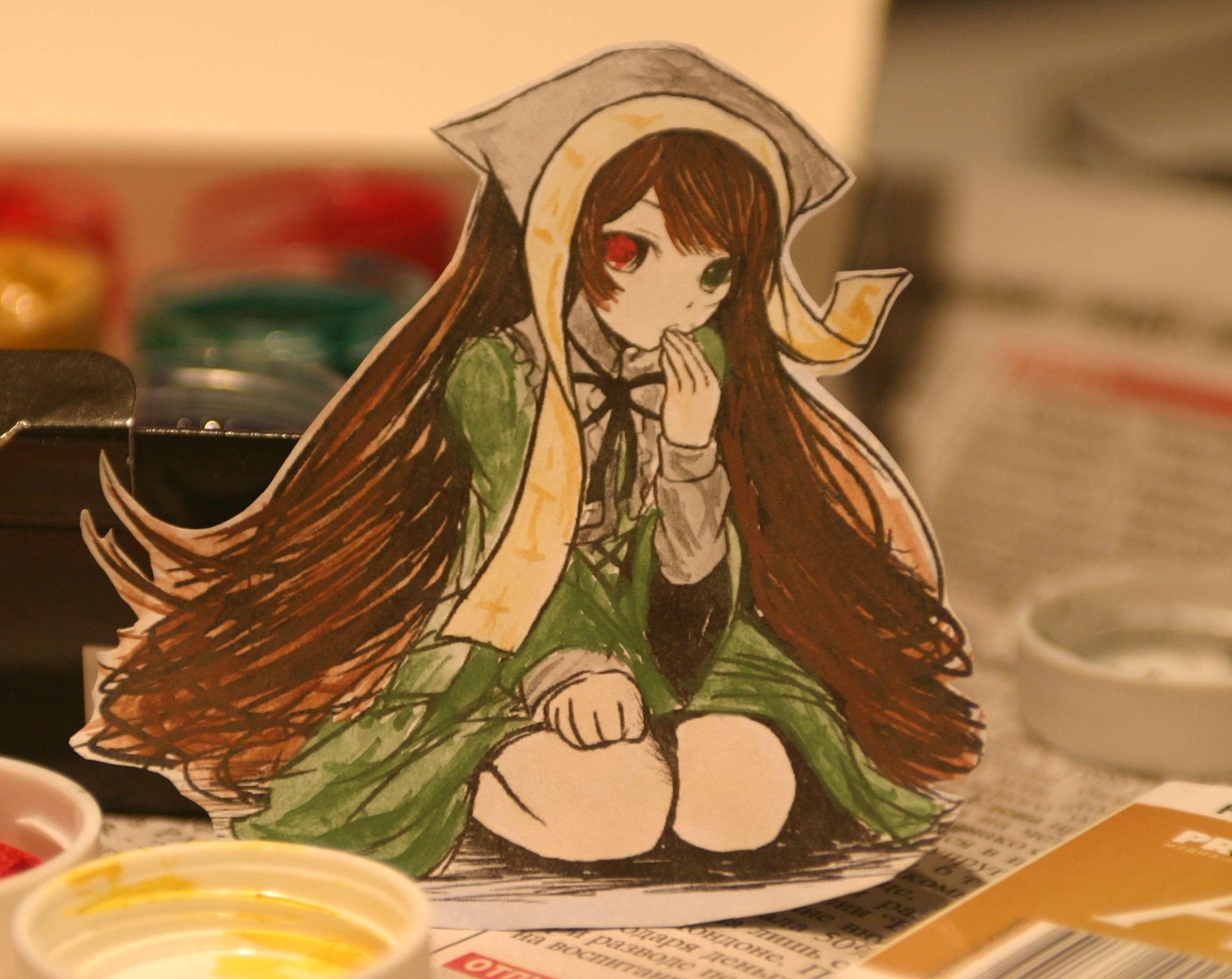 1girl blurry blurry_background blurry_foreground brown_hair depth_of_field dress food green_dress green_eyes heterochromia highres image imageboard_desourced indoors long_hair long_sleeves looking_at_viewer non-web_source paper_child papercraft_(medium) photo photo_(medium) red_eyes rozen_maiden sitting solo suiseiseki traditional_media unconventional_media very_long_hair
