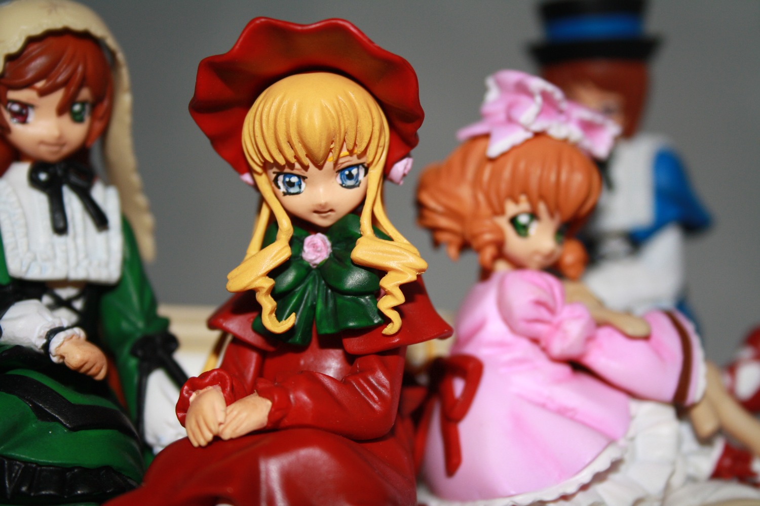 3girls blonde_hair blue_eyes blurry blurry_background blurry_foreground bonnet bow bowtie depth_of_field doll dress figure frills green_eyes hat heterochromia hina_ichigo long_hair long_sleeves looking_at_viewer motion_blur multiple_dolls multiple_girls photo pink_bow shinku sitting suiseiseki tagme v_arms