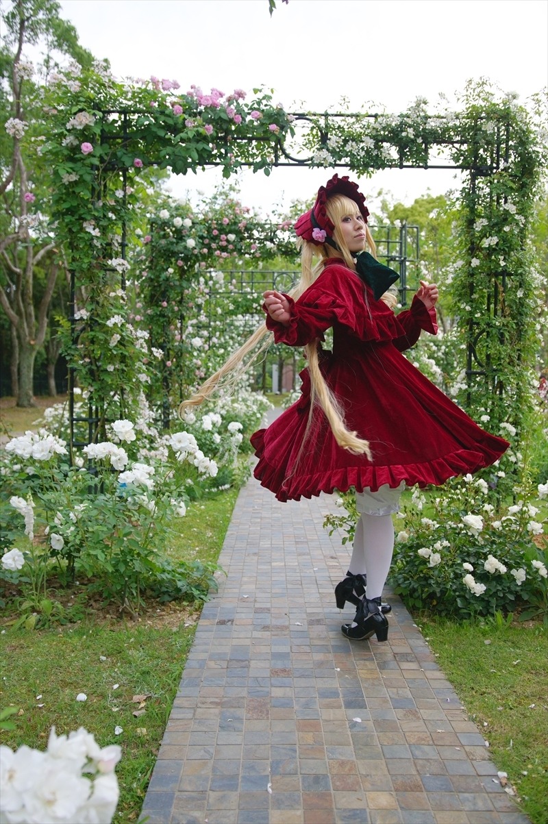 1girl black_footwear blonde_hair bow dress fence flower long_sleeves looking_back outdoors plant red_dress shinku shoes solo standing white_flower white_legwear