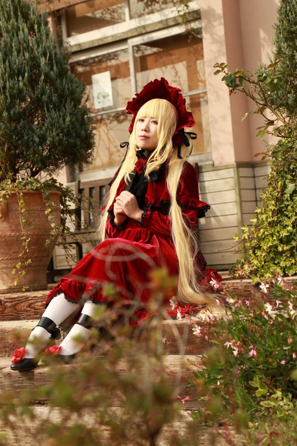 1girl blonde_hair bonnet bow doll_joints dress flower joints long_hair long_sleeves outdoors plant red_dress shinku shoes sitting solo