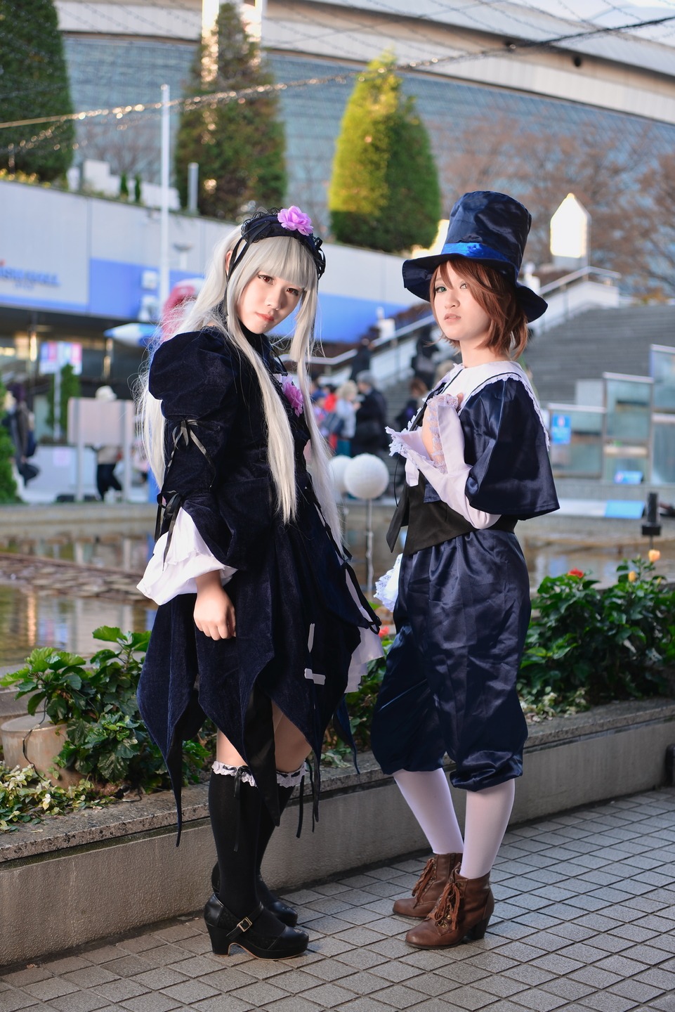 2girls black_shorts blurry boots brown_hair hat long_hair looking_at_viewer multiple_cosplay multiple_girls outdoors short_hair shorts standing tagme tile_floor