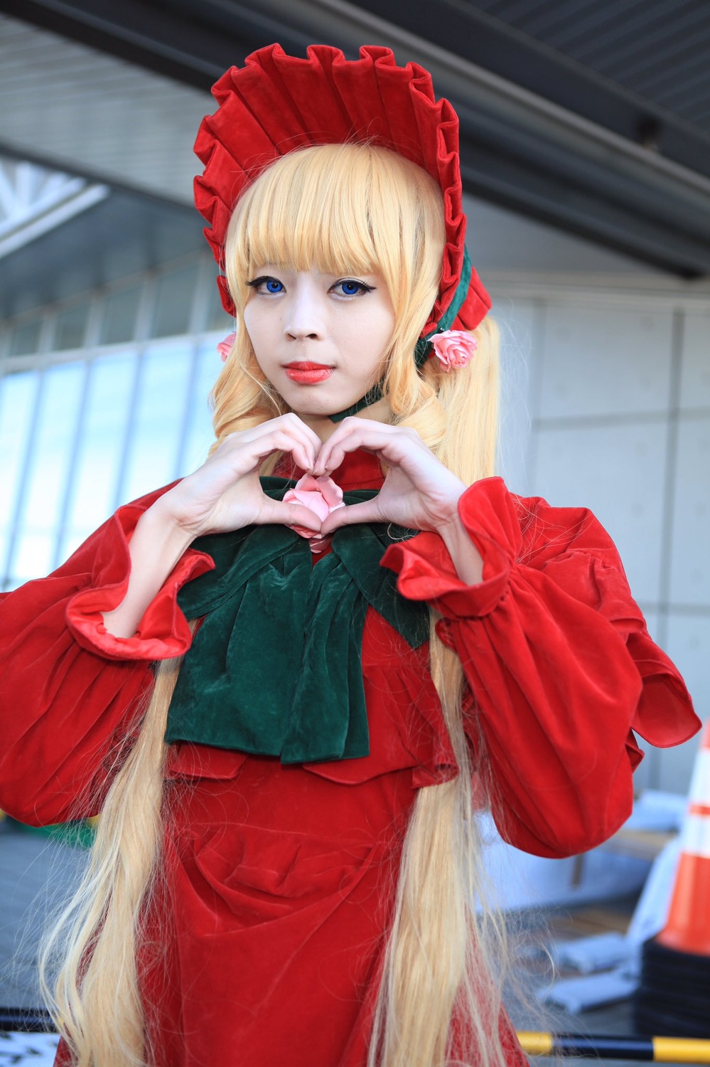 1girl blonde_hair blue_eyes blurry blurry_background bonnet bow depth_of_field dress heart heart_hands long_hair long_sleeves looking_at_viewer photo red_dress shinku solo