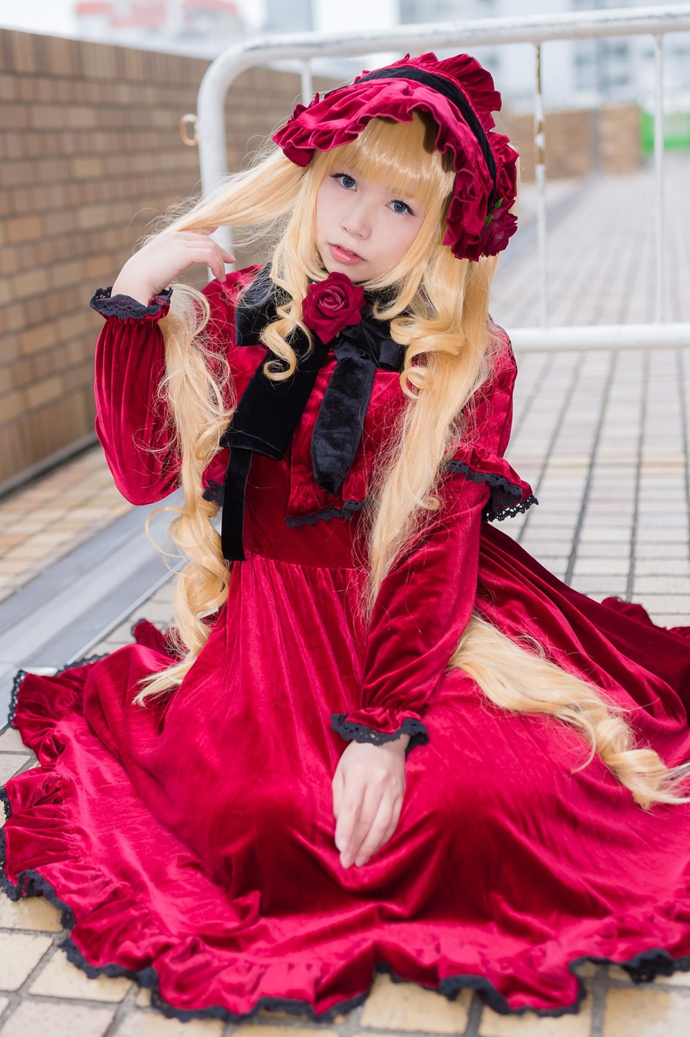 1girl blonde_hair blue_eyes blurry blurry_background bonnet depth_of_field dress flower frills lolita_fashion long_hair long_sleeves looking_at_viewer photo pink_flower pink_rose red_dress rose shinku sitting solo