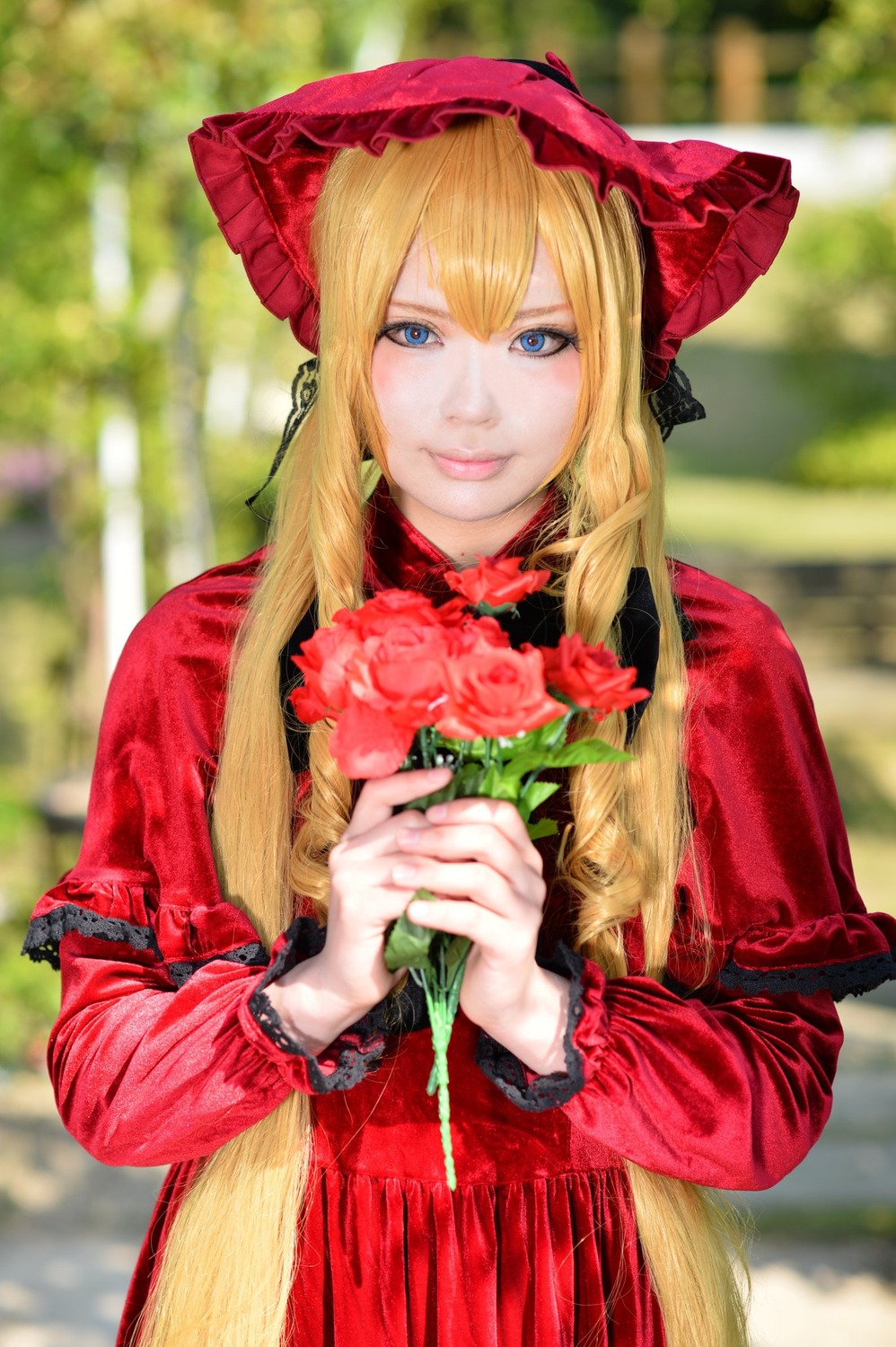 1girl bangs blonde_hair blue_eyes blurry blurry_background bonnet bouquet capelet depth_of_field dress flower holding holding_flower lips long_hair long_sleeves looking_at_viewer photo red_capelet red_dress red_flower rose shinku smile solo upper_body