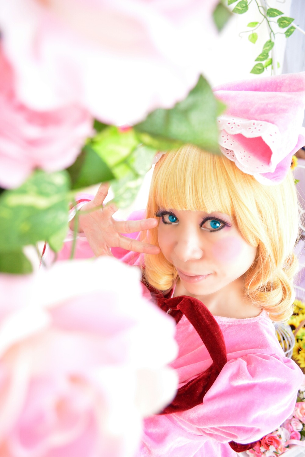 1girl bangs blonde_hair blue_eyes blunt_bangs blurry blurry_background blurry_foreground depth_of_field dress flower hinaichigo lips looking_at_viewer lying motion_blur photo pink_dress plant solo