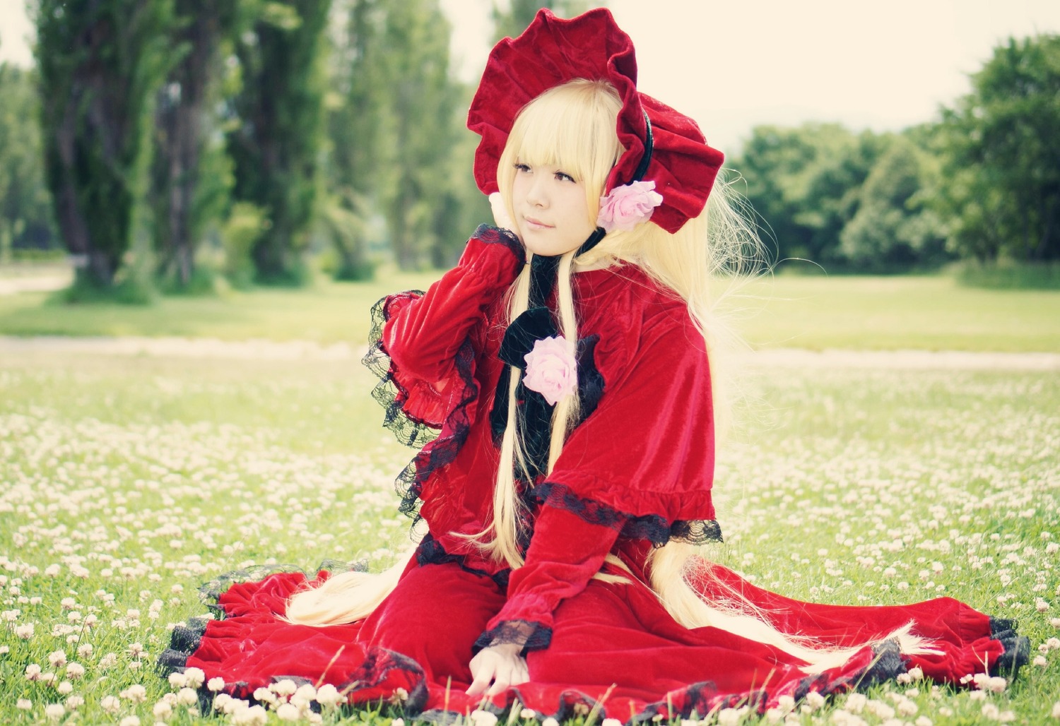 1girl blonde_hair blue_eyes blurry bonnet bow dress field flower frills garden grass long_hair long_sleeves outdoors red_dress shinku sitting solo