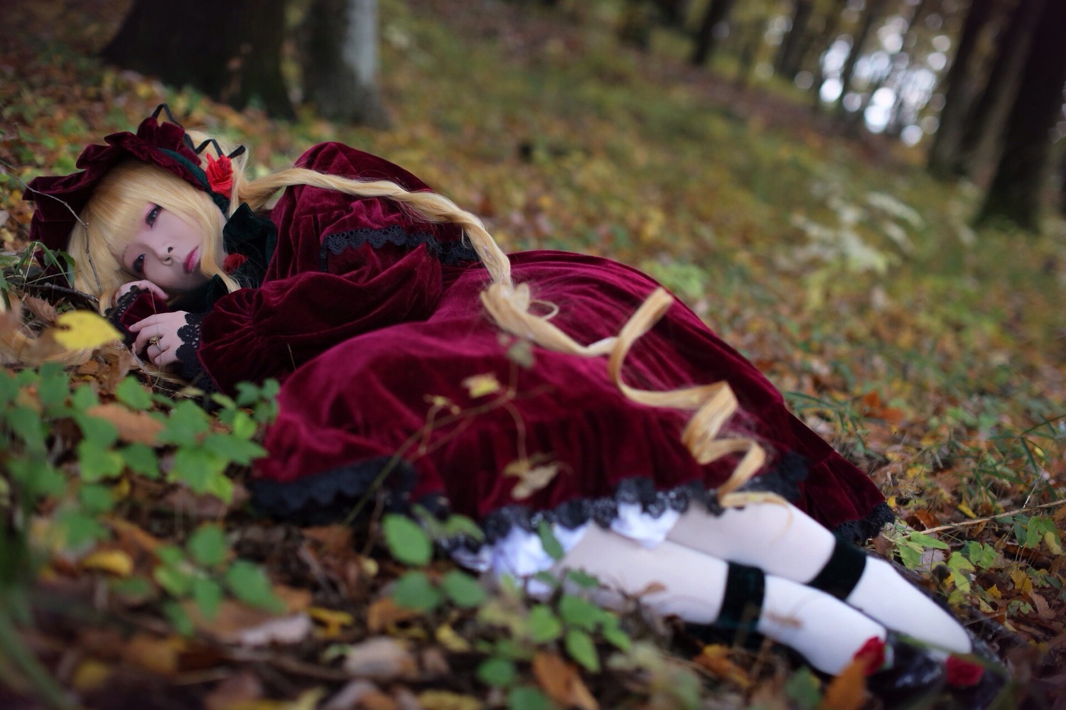 1girl blonde_hair blurry blurry_background blurry_foreground bonnet bow depth_of_field dress long_sleeves lying on_side red_dress ribbon shinku sleeping solo twintails