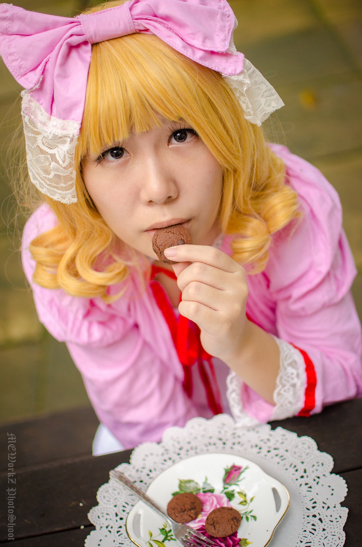 1girl blonde_hair blurry blurry_background bow depth_of_field food hair_bow hinaichigo lips long_hair looking_at_viewer photo pink_bow pink_dress plate realistic solo table