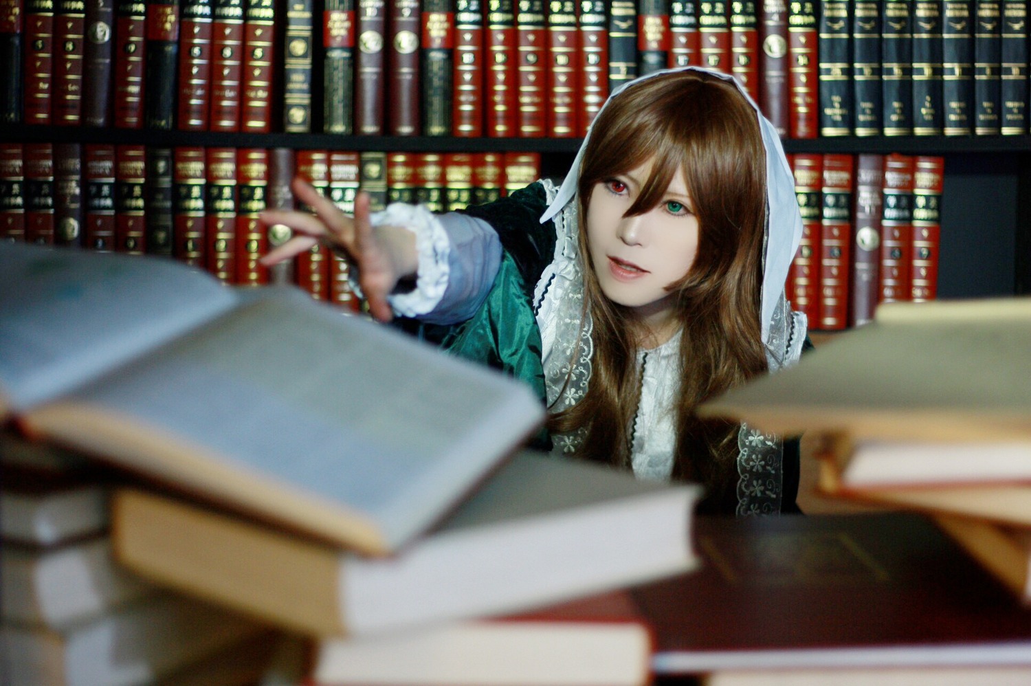1girl 3d blurry blurry_background blurry_foreground book book_stack bookshelf brown_hair depth_of_field green_eyes heterochromia library lips long_hair looking_at_viewer motion_blur red_eyes shirt solo