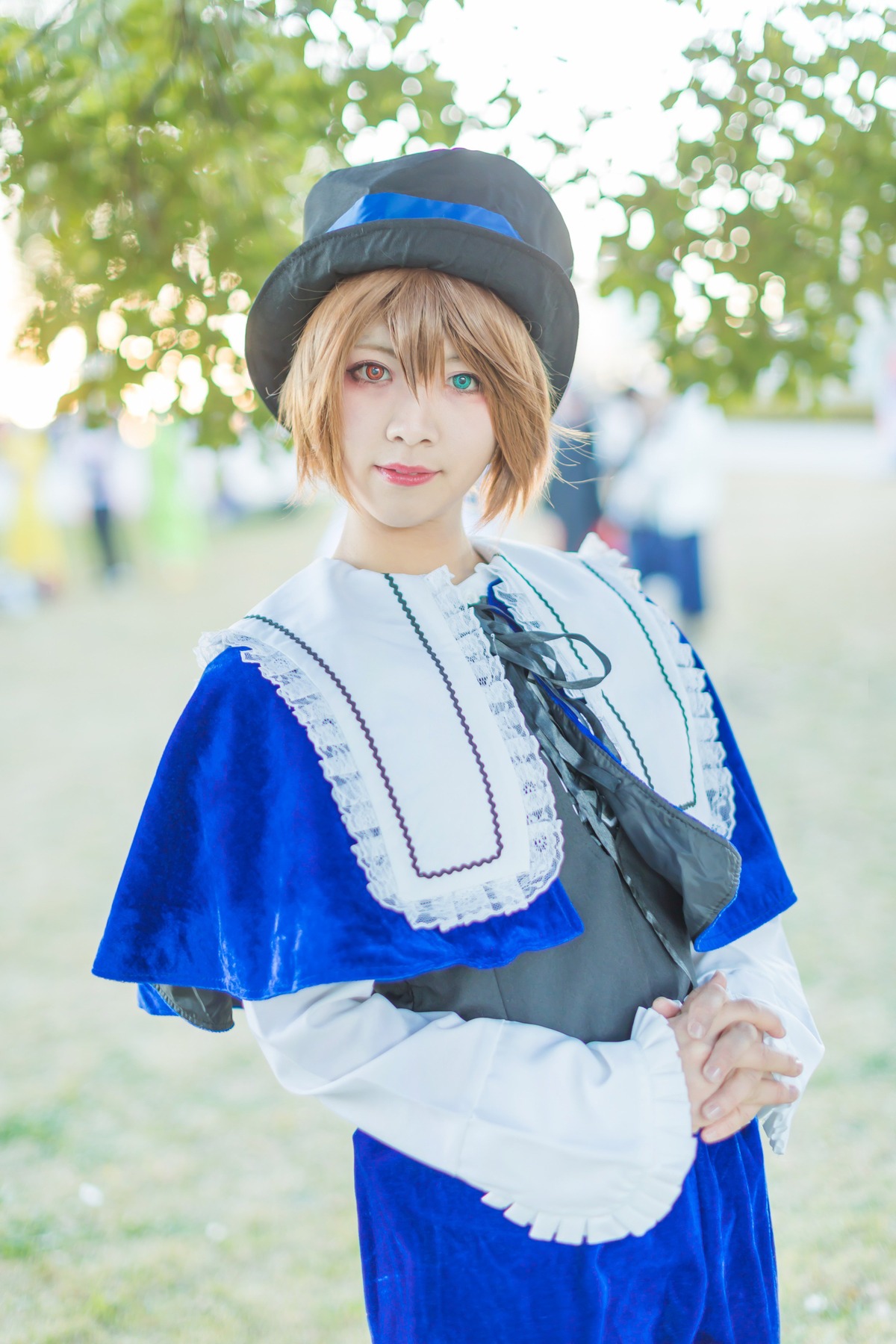 1girl blonde_hair blue_dress blue_eyes blue_headwear blue_ribbon blurry blurry_background capelet depth_of_field dress hat lips long_sleeves looking_at_viewer outdoors photo realistic ribbon short_hair skirt solo souseiseki