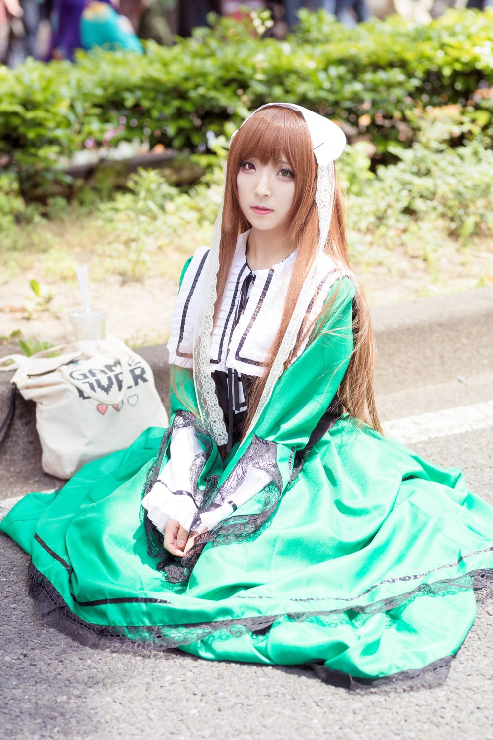 1girl bangs blurry blurry_background brown_hair day depth_of_field dress green_dress lips long_hair looking_at_viewer outdoors photo sitting solo suiseiseki