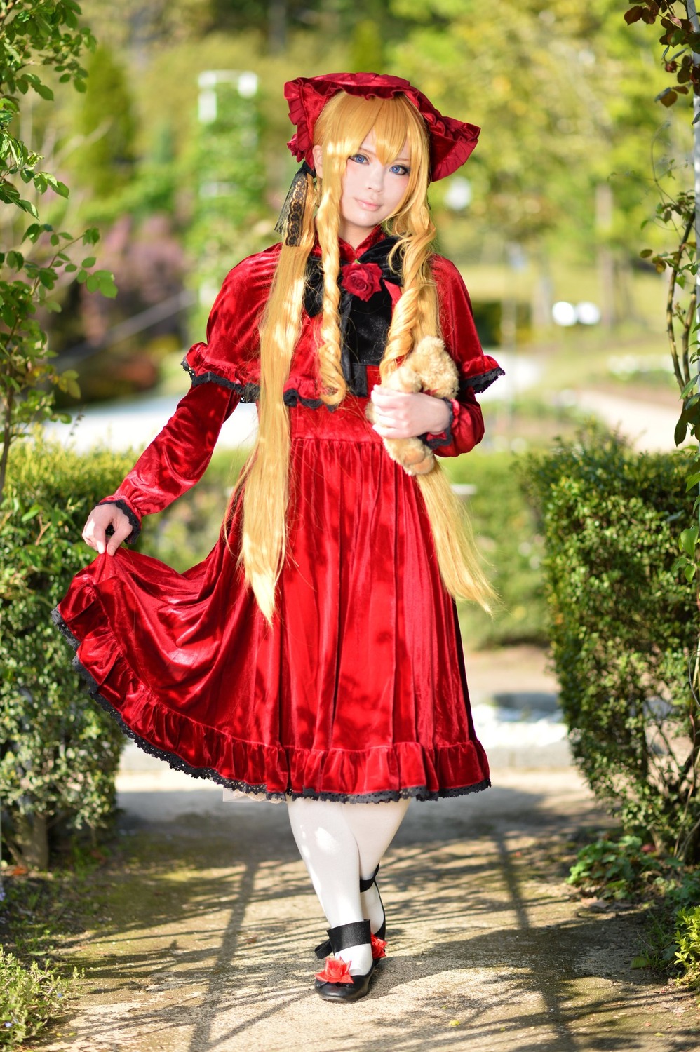 1girl blonde_hair blue_eyes blurry bonnet bow bush depth_of_field dress flower long_hair looking_at_viewer outdoors pantyhose plant red_dress shinku shoes solo standing white_legwear