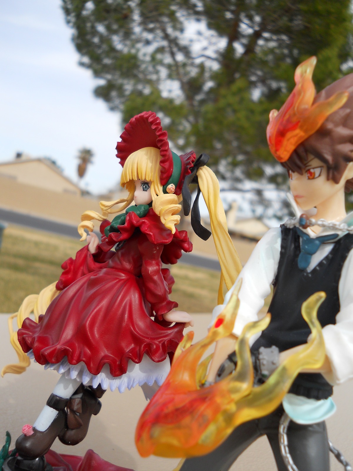 1boy 1girl blonde_hair blurry blurry_background blurry_foreground bonnet bow depth_of_field doll dress drill_hair frills long_hair long_sleeves outdoors photo shinku solo standing
