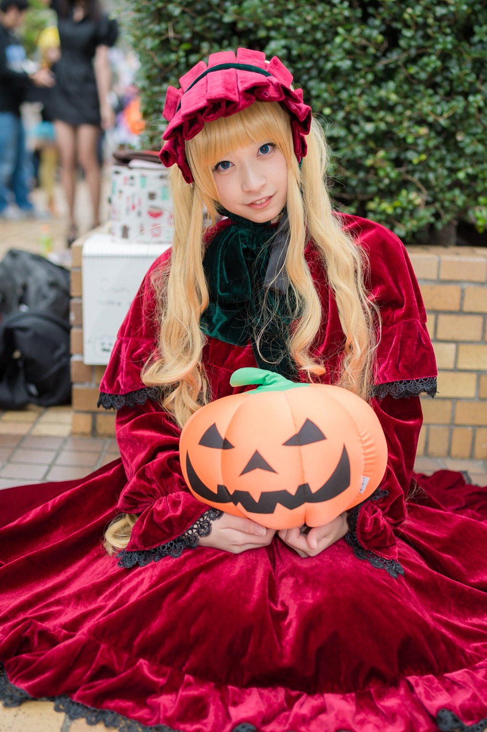 1girl blonde_hair blue_eyes blurry blurry_background blurry_foreground depth_of_field dress frills jack-o'-lantern lolita_fashion long_hair long_sleeves looking_at_viewer photo pumpkin red_dress shinku sitting smile solo solo_focus