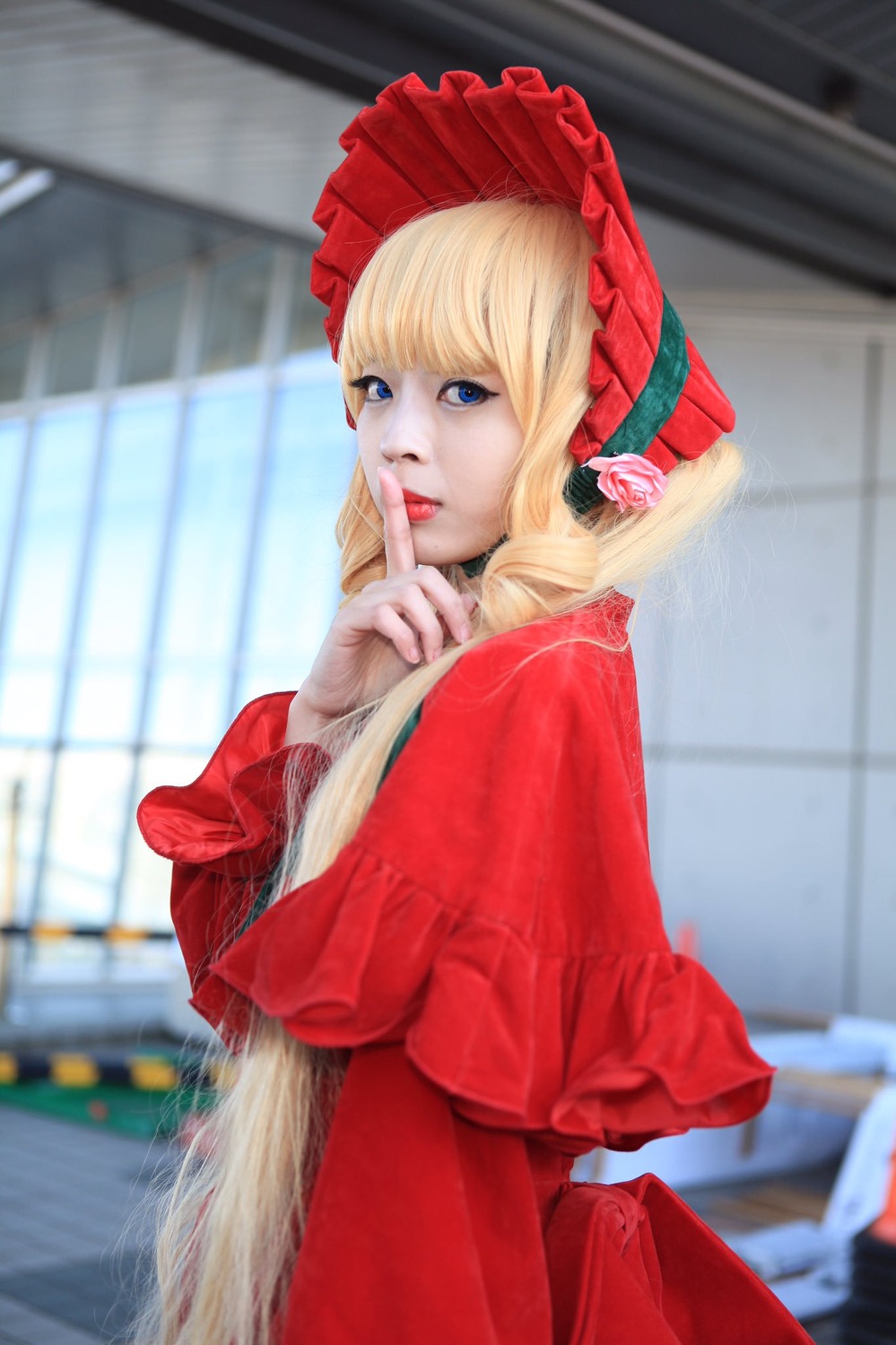 1girl bangs blonde_hair blue_eyes blurry blurry_background blurry_foreground bonnet depth_of_field dress finger_to_mouth looking_at_viewer photo red_dress shinku solo