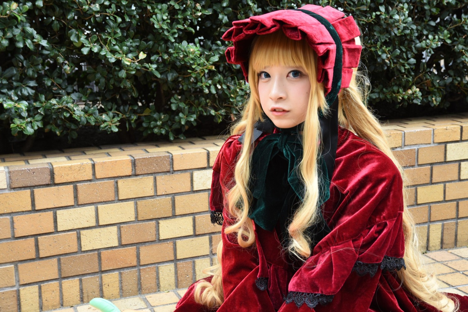 1girl bangs blonde_hair blue_eyes bonnet brick_wall bush day dress lips long_hair long_sleeves looking_at_viewer outdoors red_dress shinku solo upper_body wall