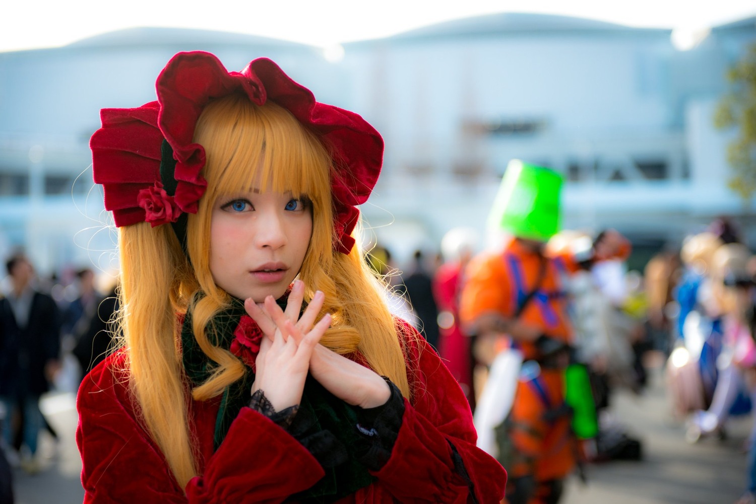 1girl bangs blonde_hair blue_eyes blurry blurry_background blurry_foreground bonnet depth_of_field dress flower hat lips long_hair looking_at_viewer own_hands_together photo red_flower red_rose rose shinku solo solo_focus