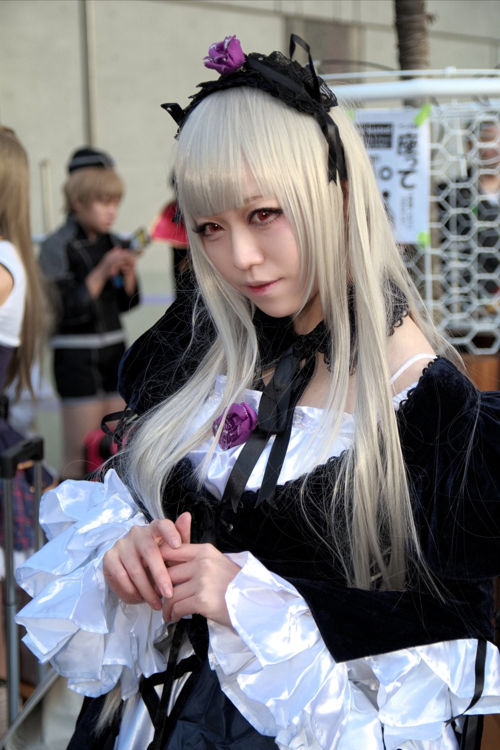 1girl bangs blonde_hair blurry blurry_background blurry_foreground depth_of_field dress figure flower frills gothic_lolita hairband hat lips lolita_fashion long_hair long_sleeves multiple_girls photo red_eyes solo solo_focus suigintou