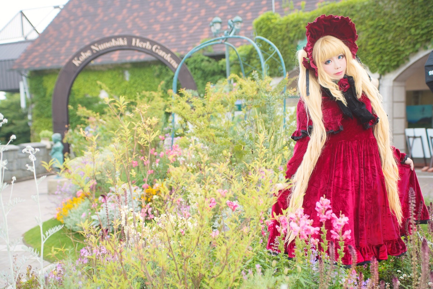 1girl blonde_hair blue_eyes blurry bonnet day dress flower long_hair long_sleeves looking_at_viewer outdoors red_dress shinku solo standing umbrella