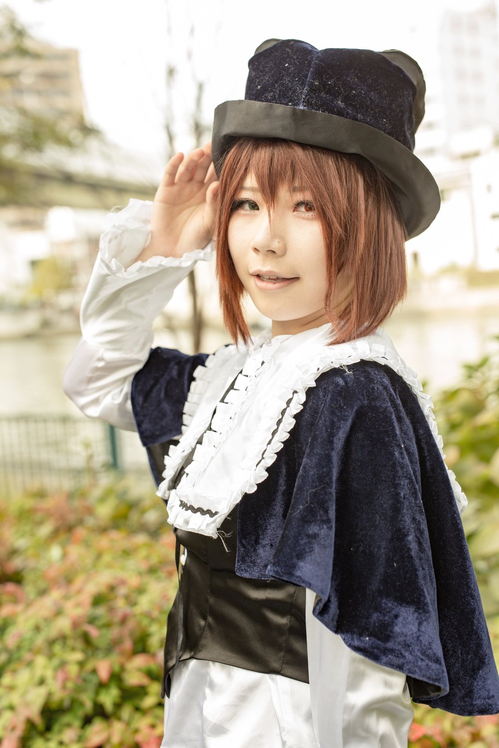 1girl blurry blurry_background brown_eyes brown_hair capelet depth_of_field hat long_sleeves looking_at_viewer outdoors photo_background short_hair smile solo souseiseki