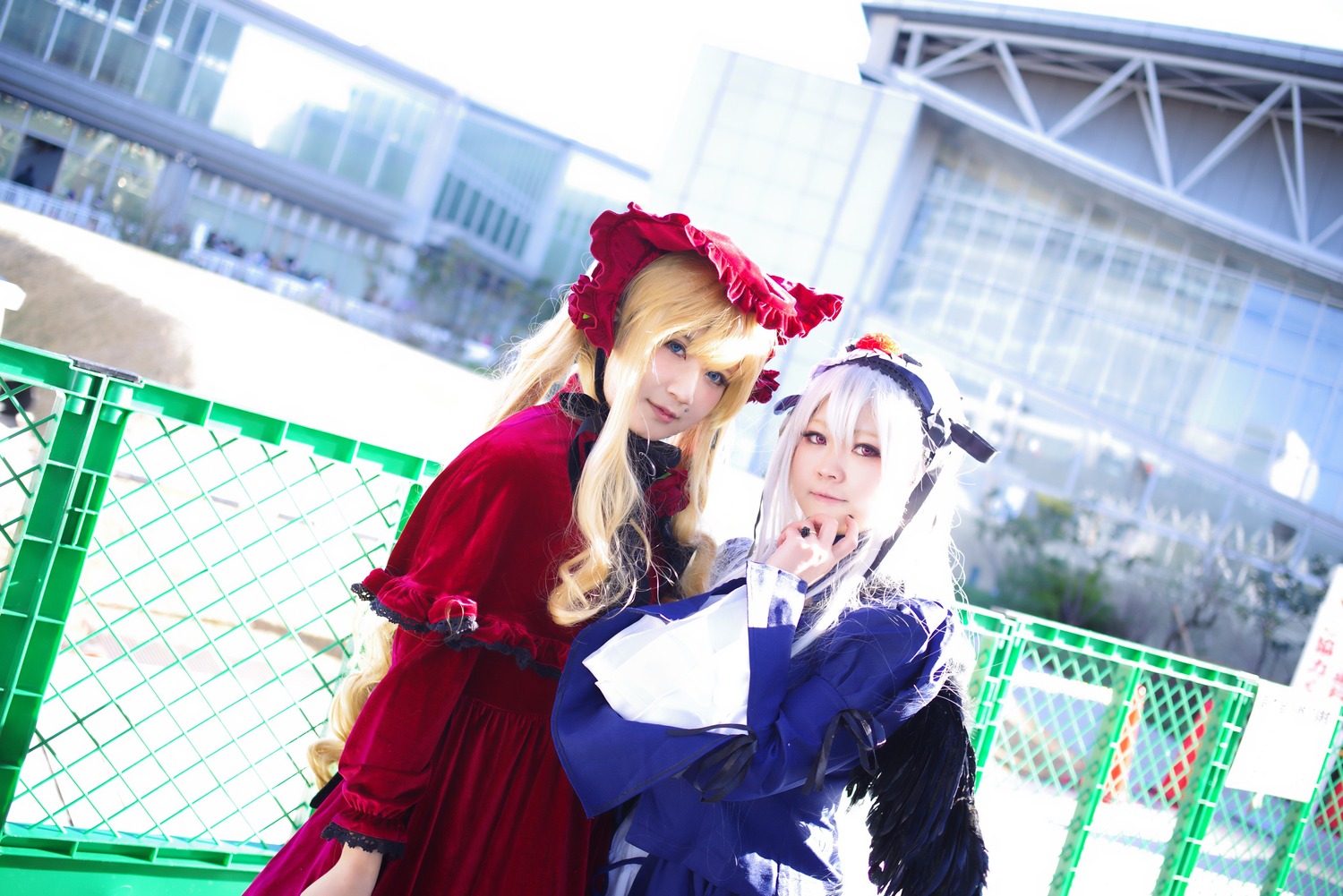 2girls blonde_hair blurry bonnet building city depth_of_field dress fence indoors long_hair looking_at_another multiple_cosplay multiple_girls tagme