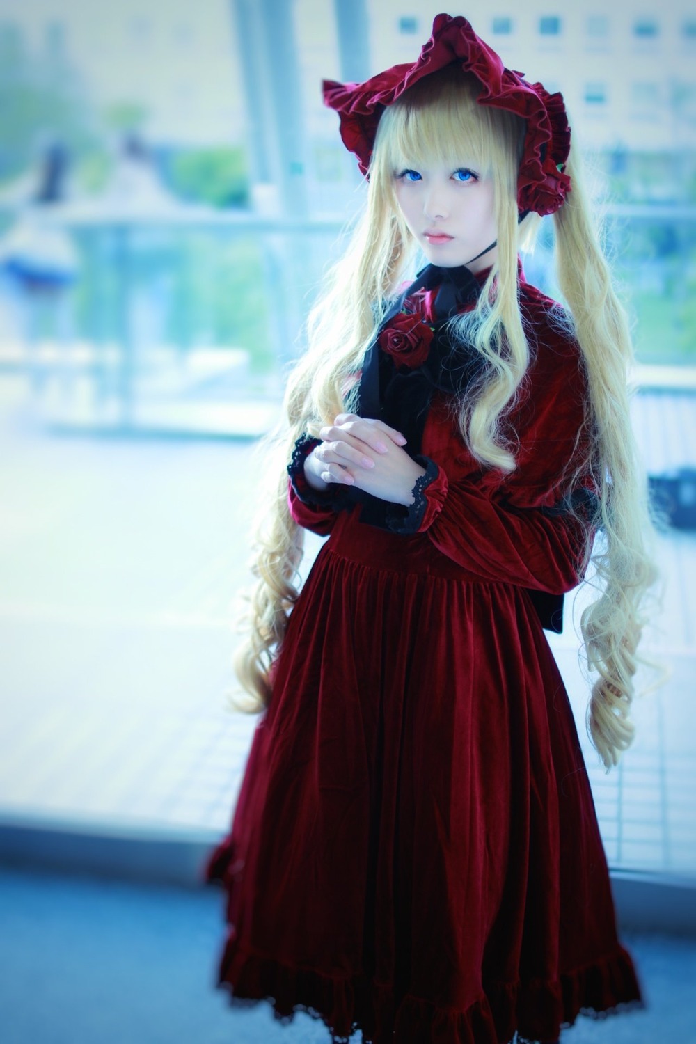 1girl blonde_hair blue_eyes blurry blurry_background blurry_foreground bonnet depth_of_field dress flower long_hair long_sleeves looking_at_viewer photo red_dress shinku solo standing