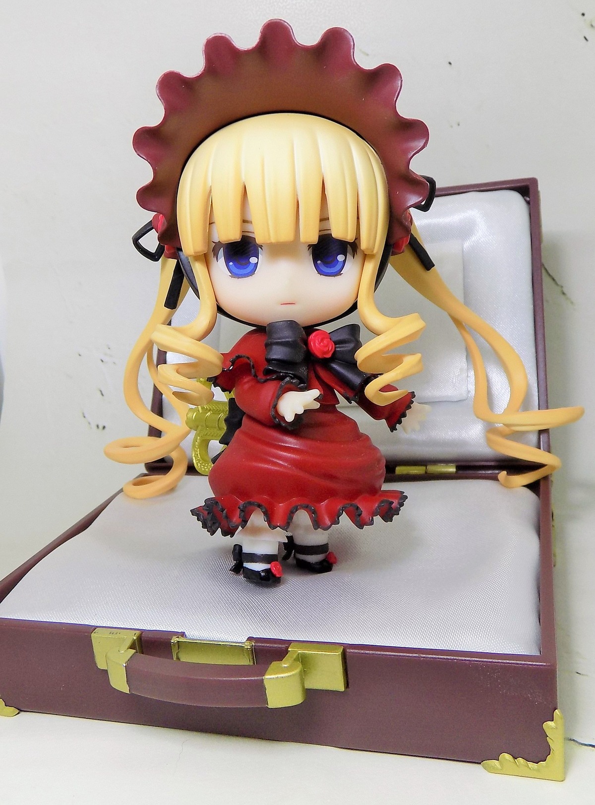 1girl blonde_hair blue_eyes bonnet bow bowtie chibi cup doll dress drill_hair figure long_hair long_sleeves looking_at_viewer photo red_dress shinku shoes solo standing suitcase twintails