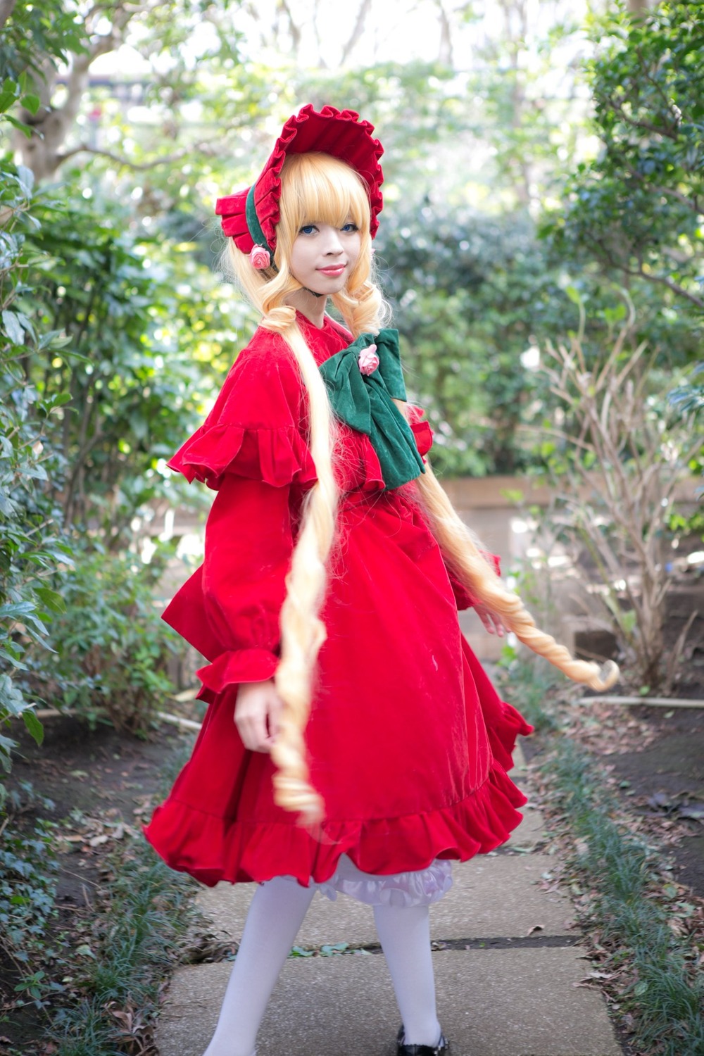 1girl blonde_hair blue_eyes blurry bonnet bow capelet depth_of_field dress outdoors pantyhose realistic red_dress shinku shoes solo standing white_legwear