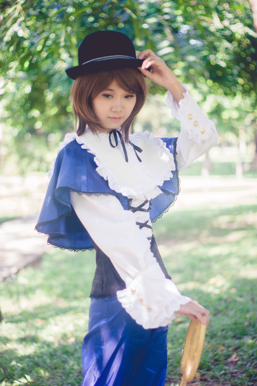 1girl blue_dress blurry brown_hair capelet day depth_of_field dress grass hat long_sleeves outdoors pants realistic ribbon smile solo souseiseki standing sunlight